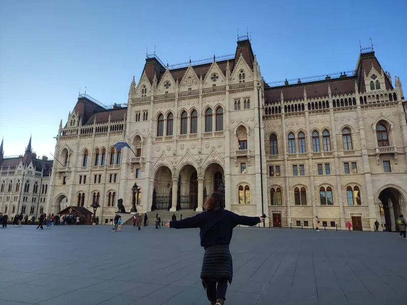 Devant la façade du Parlement hongrois, bras écartés