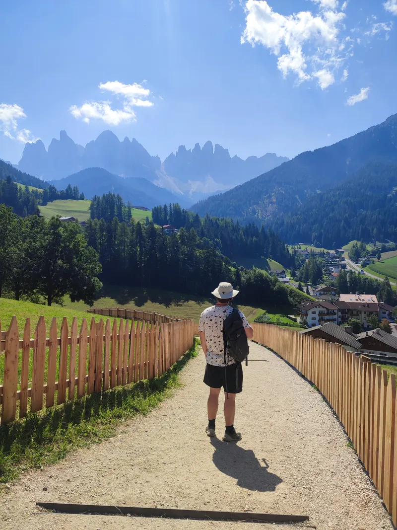 Chemin longeant une palissade de bois, aiguilles rocheuses au fond